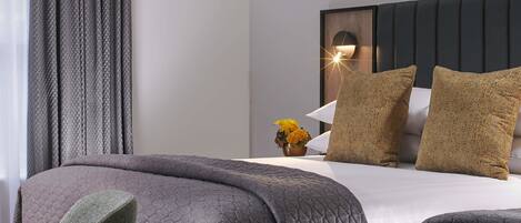 A neatly made bed with a quilted cover, a bedside table with a vase of flowers, and a wall-mounted light fixture.