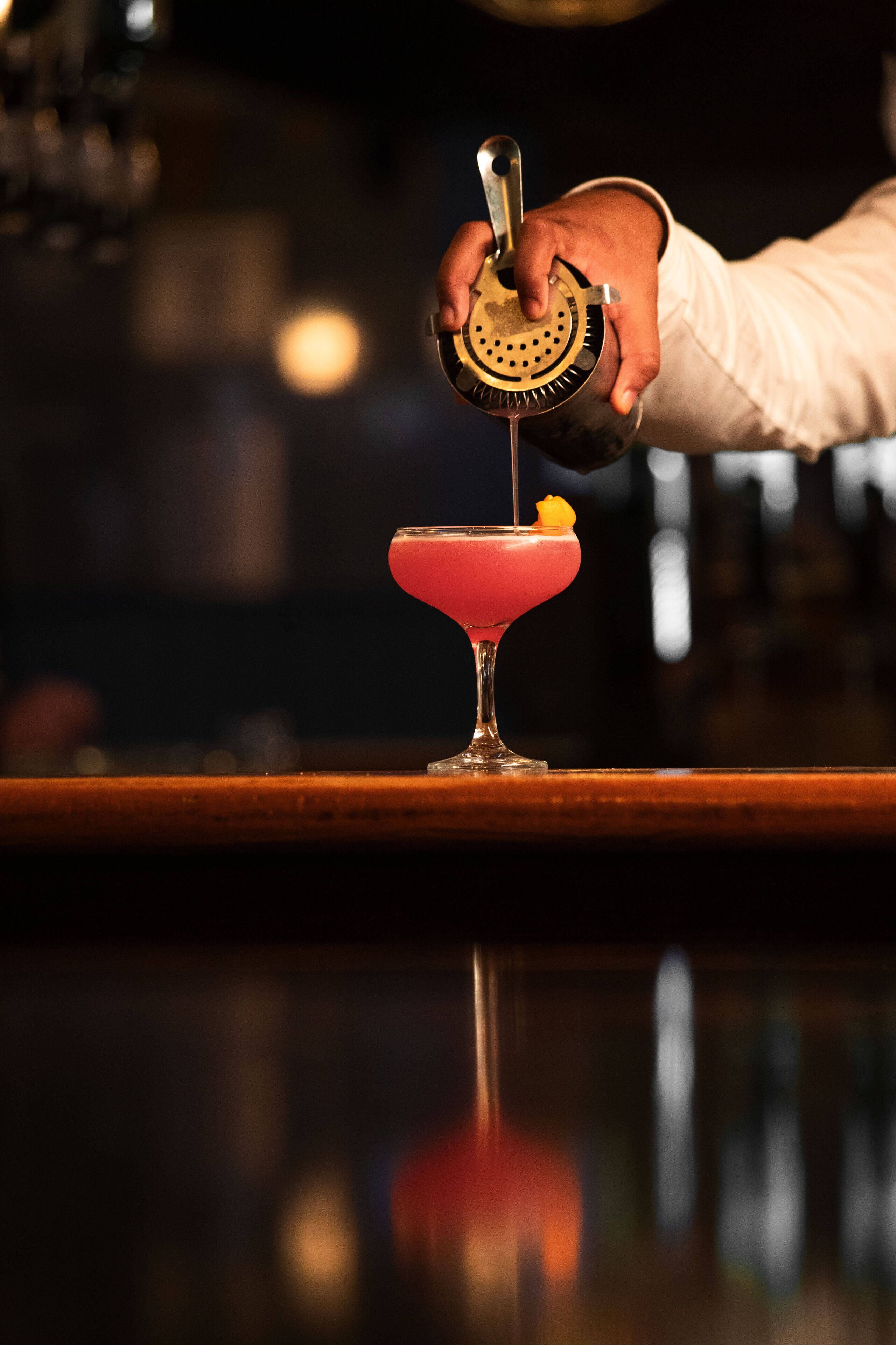 A bartender pouring a drink into a martini glass.