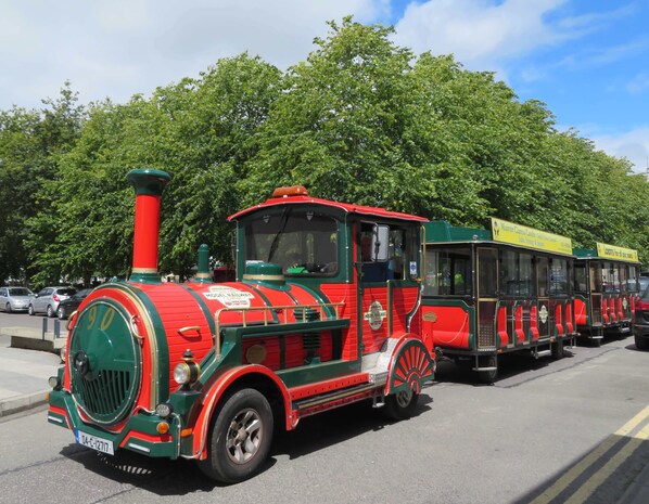 A vintage red and green train with a number 90 on the front, parked on a street with trees in the background.
