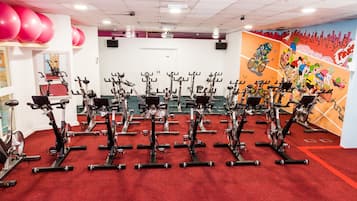 A gym with stationary bikes arranged in rows, a red carpet, and a colorful mural on the wall.