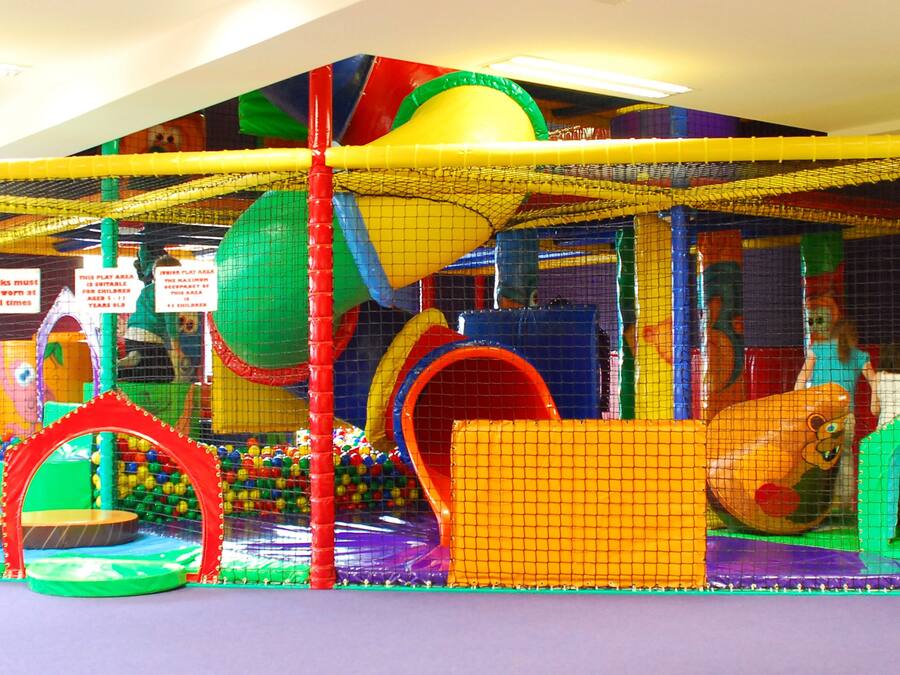 A colorful indoor play area with various play structures and safety nets.