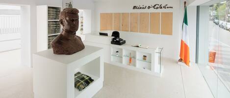 Un interior moderno con un mostrador de recepción blanco, un busto, una estantería y una vitrina de vidrio.
