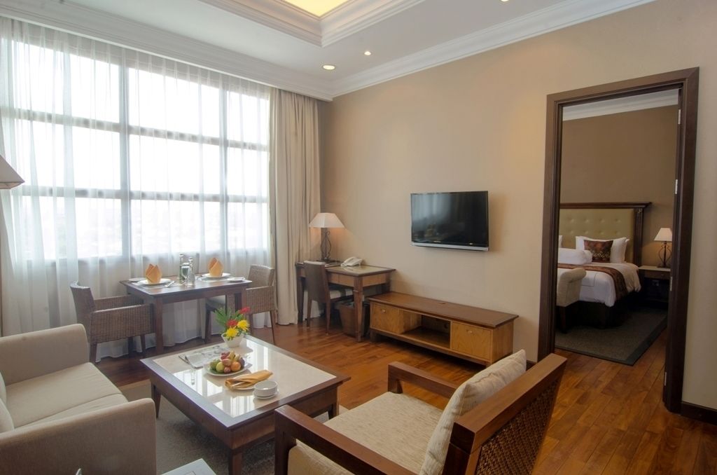 A hotel room with a dining area, a TV, a bed, and a large mirror.