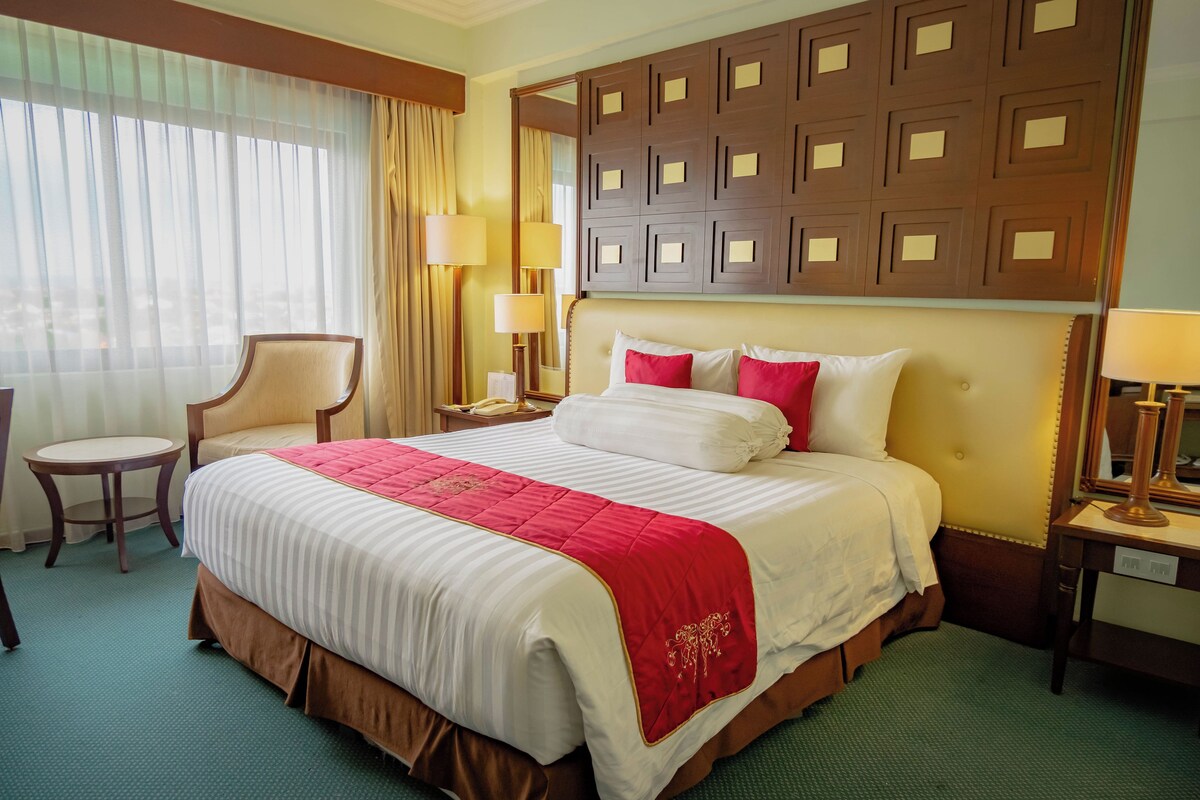 A hotel room with a large bed, a chair, a nightstand, and a mirror.