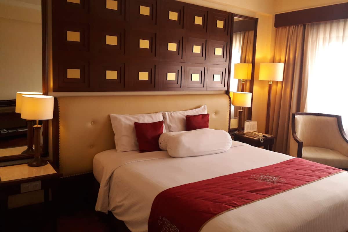 A hotel room with a large bed, two bedside lamps, a chair, and a decorative headboard.
