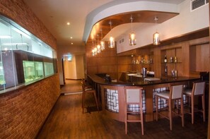 Un espace bar doté d’un comptoir incurvé, de lambris en bois, de luminaires suspendus et d’une vitrine.