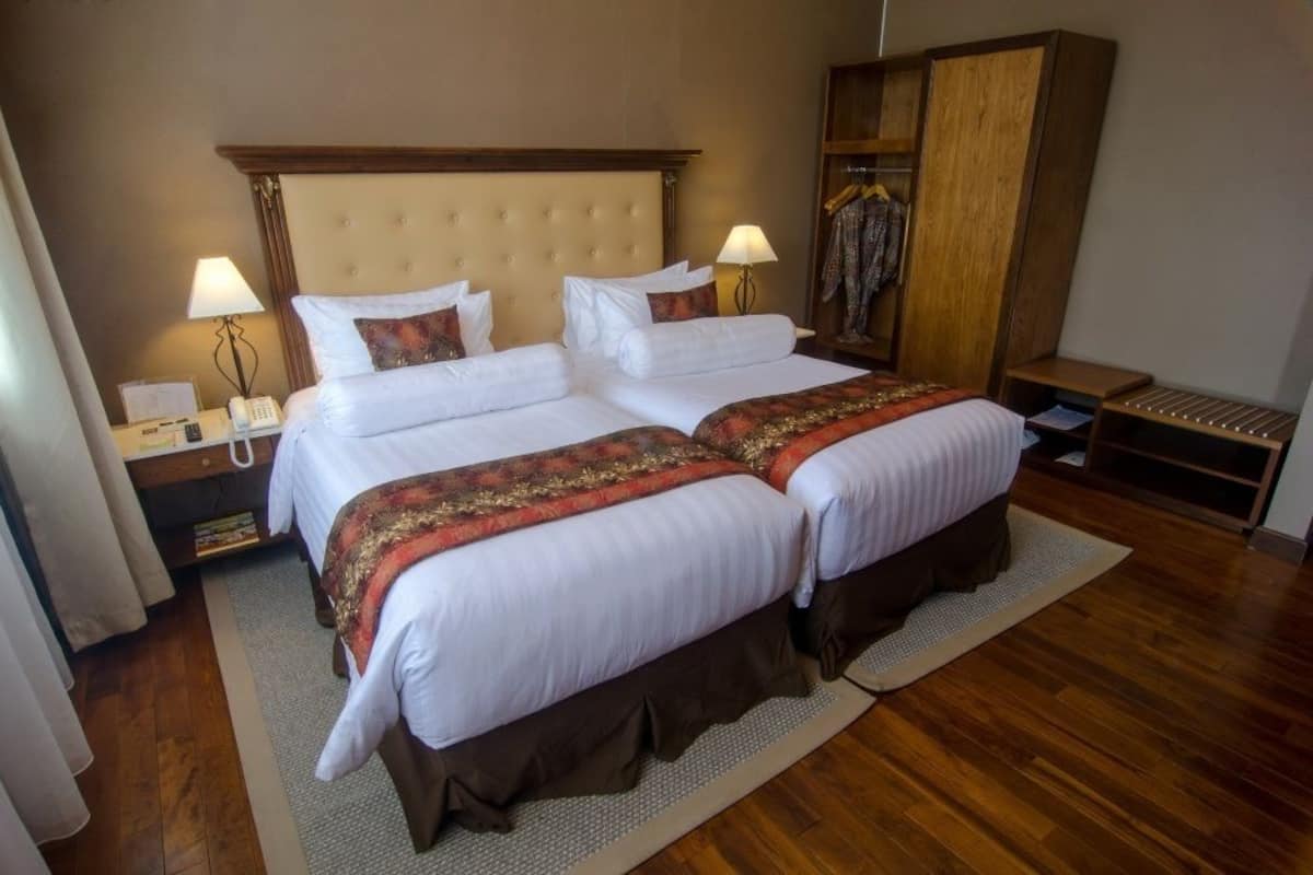 A double bed with a tufted headboard, two bedside tables with lamps, a wardrobe, and a wooden floor.