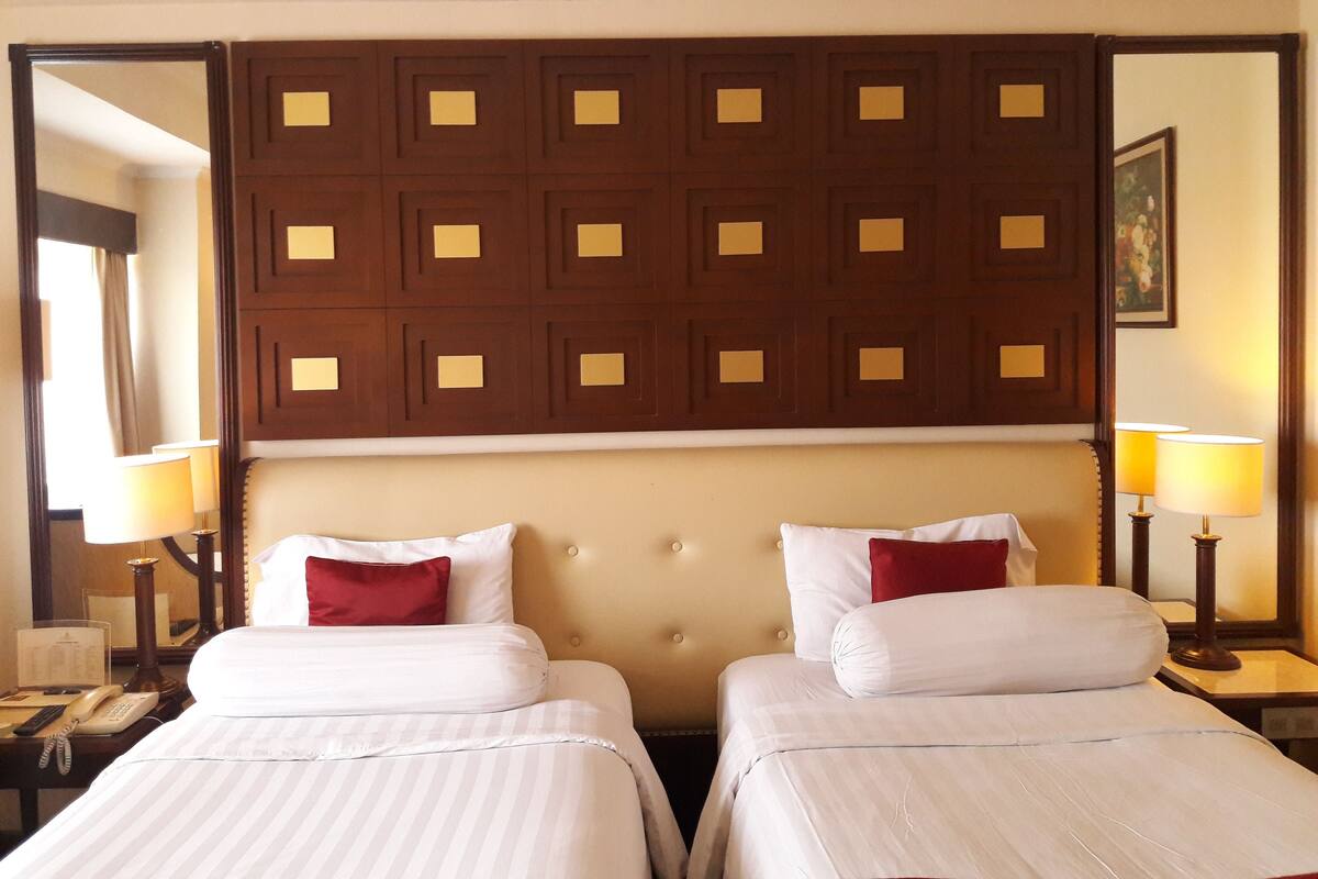 A hotel room with two beds, a wooden headboard, bedside lamps, and a telephone on the nightstand.