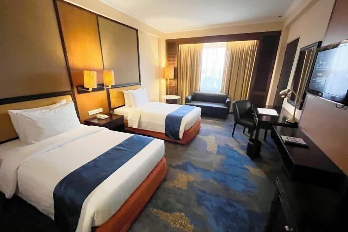Een hotelkamer met twee bedden, een bureau, een stoel, een televisie en een groot raam met gordijnen.