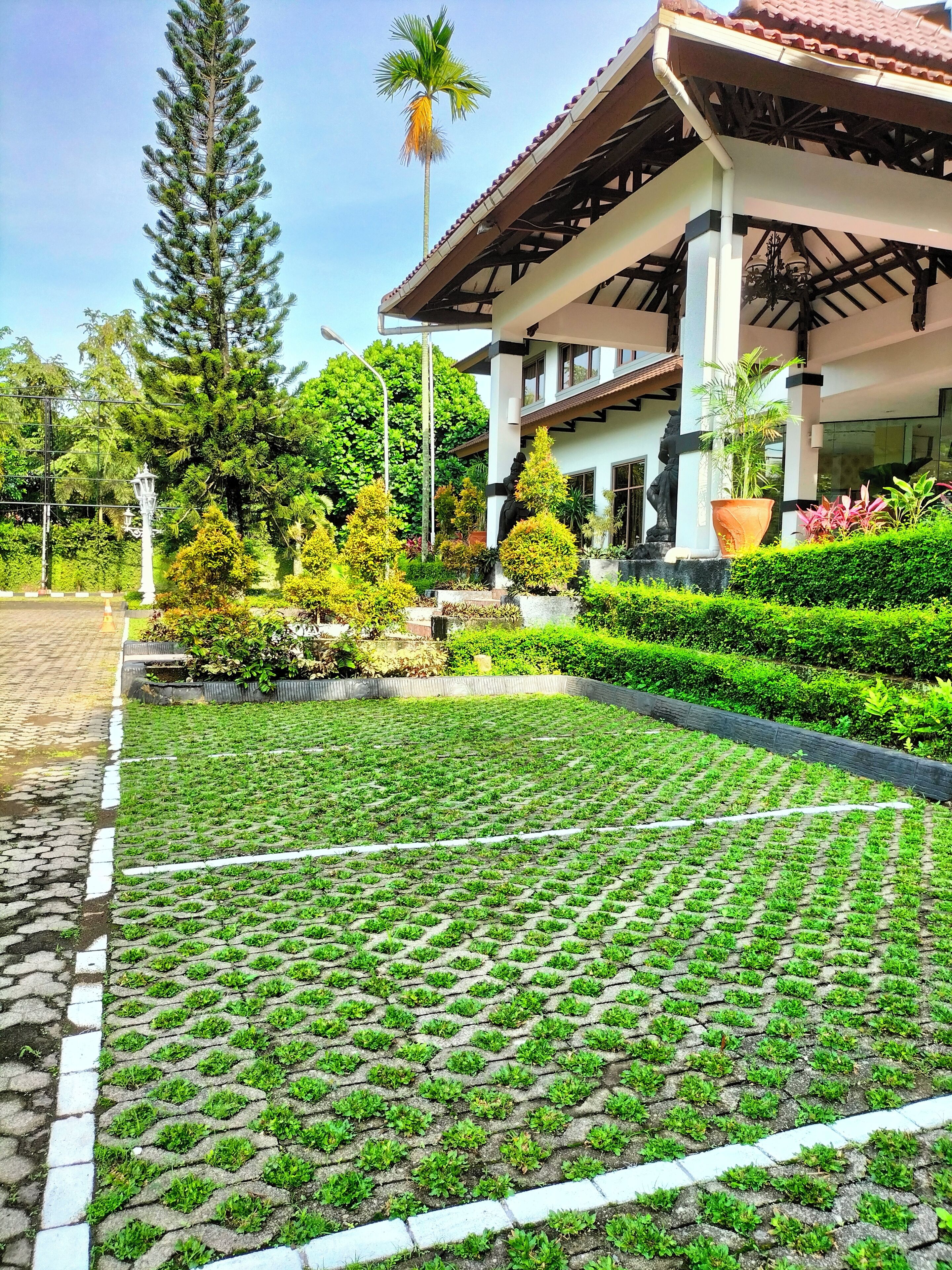 Un jardin bien entretenu, agrémenté d’une zone pavée, d’une statue et d’un bâtiment doté d’un toit en tuiles et de colonnes.
