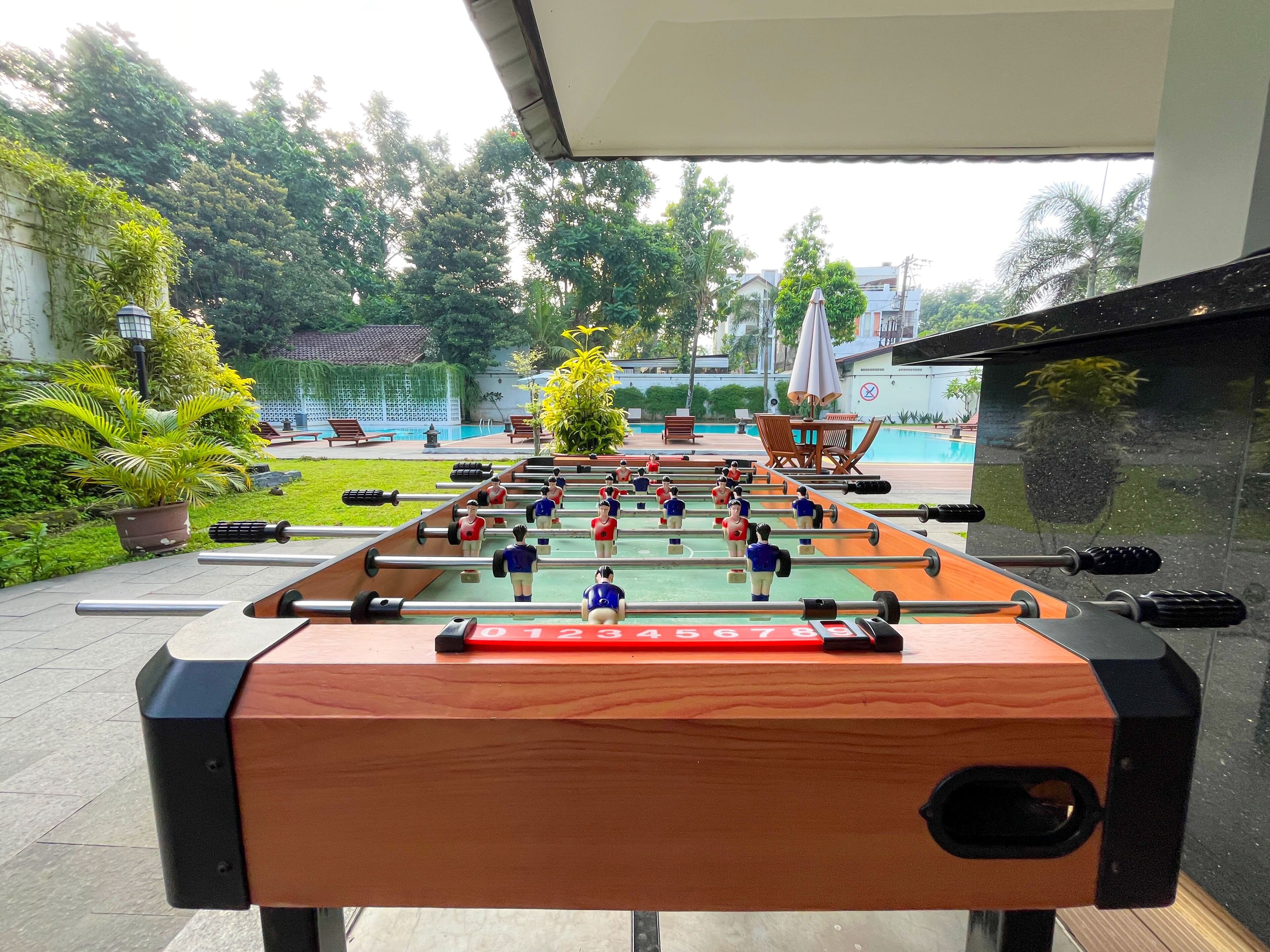 A foosball table in an outdoor setting with a pool and greenery in the background.