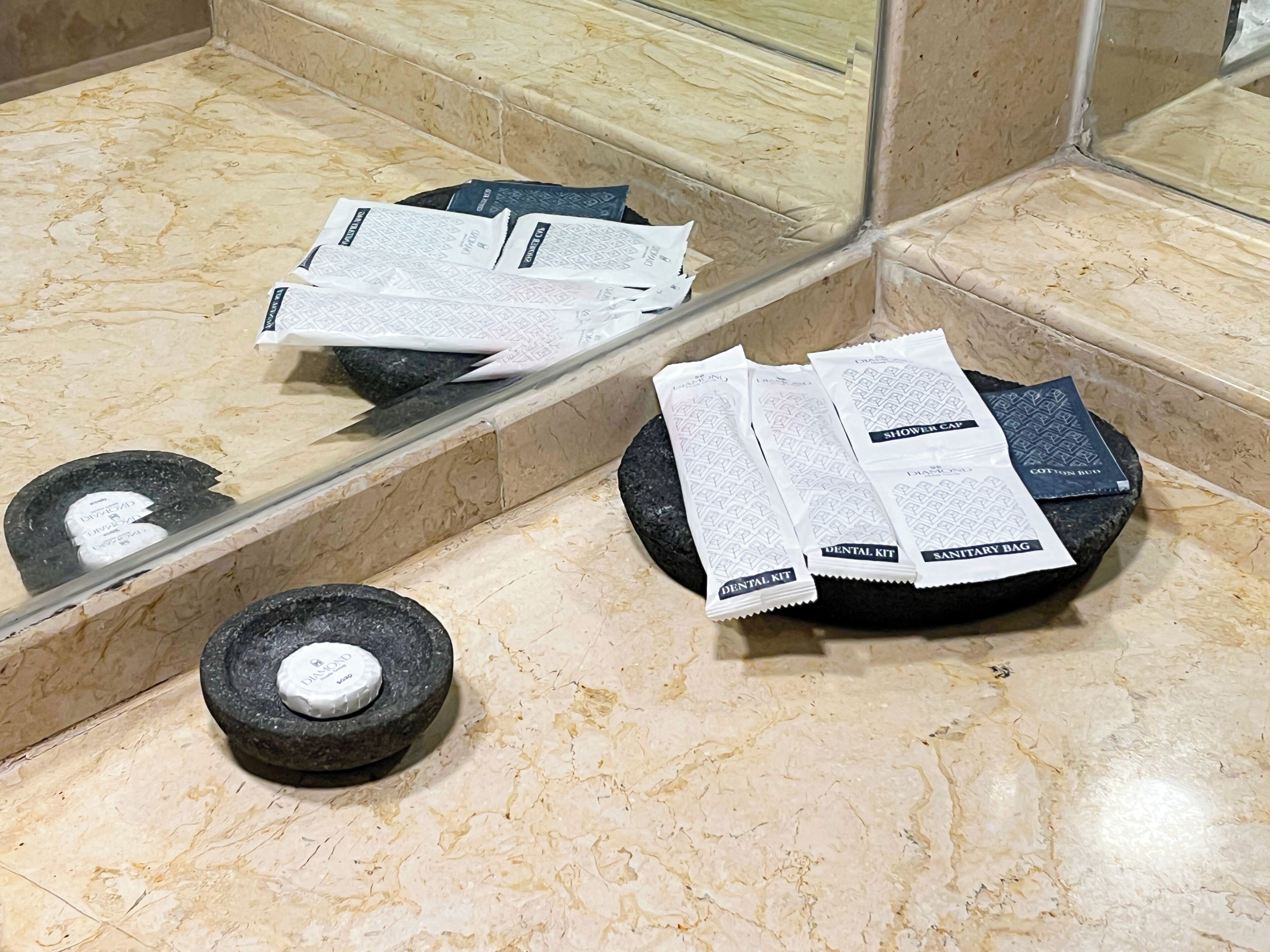 A bathroom with a marble floor, a mirror, and toiletries including a dental kit, sanitary bag, and cotton buds.