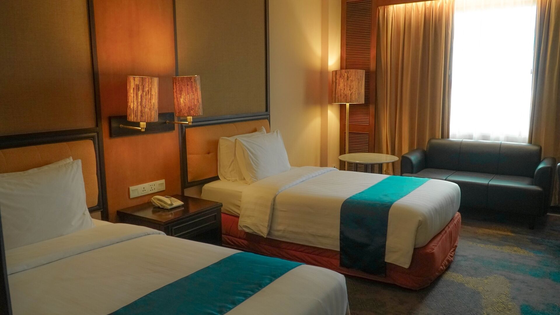Habitación de hotel con dos camas, una mesita pequeña, una silla y una lámpara.