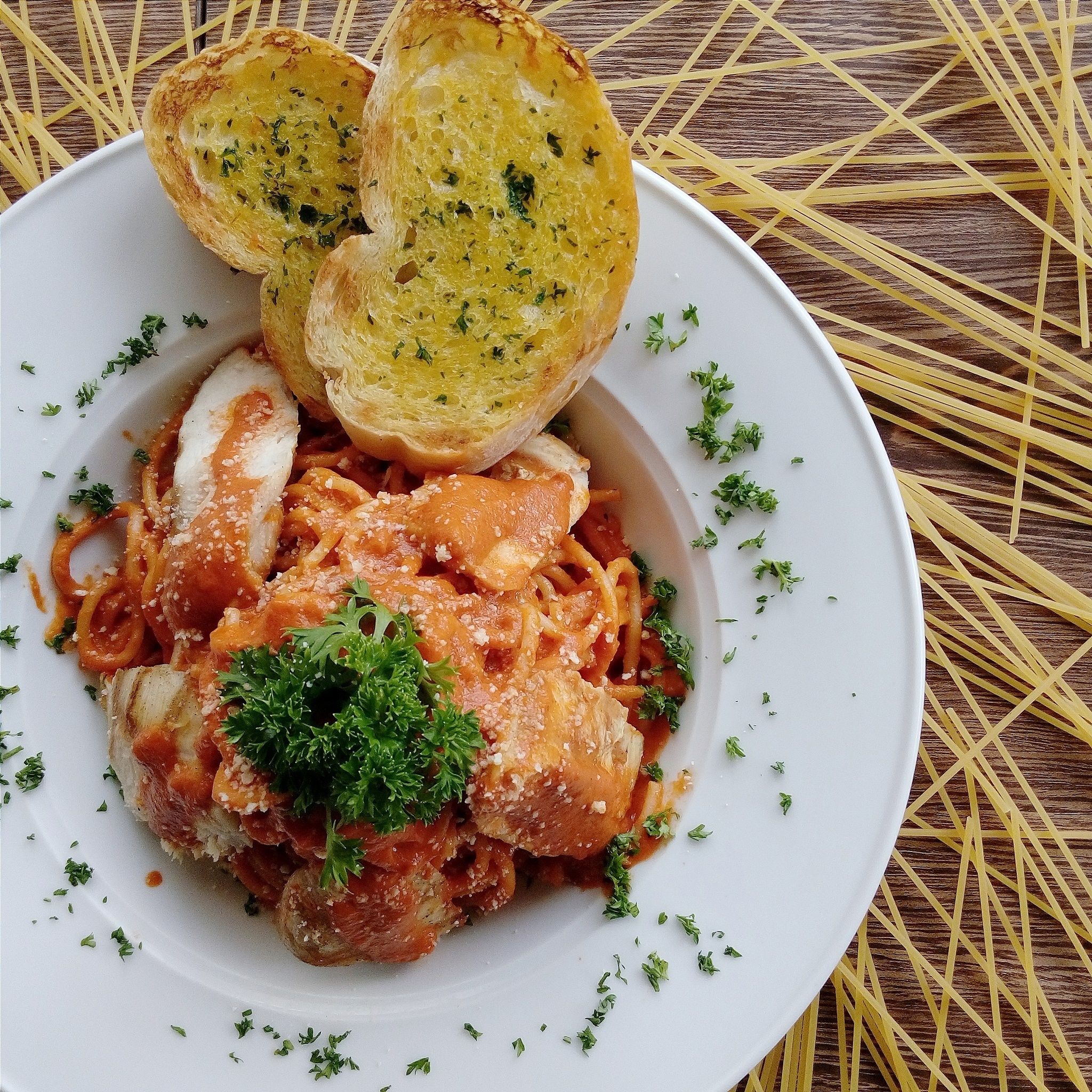 En tallrik pasta med en garnering, serverad tillsammans med två bitar vitlöksbröd på ett träbord.