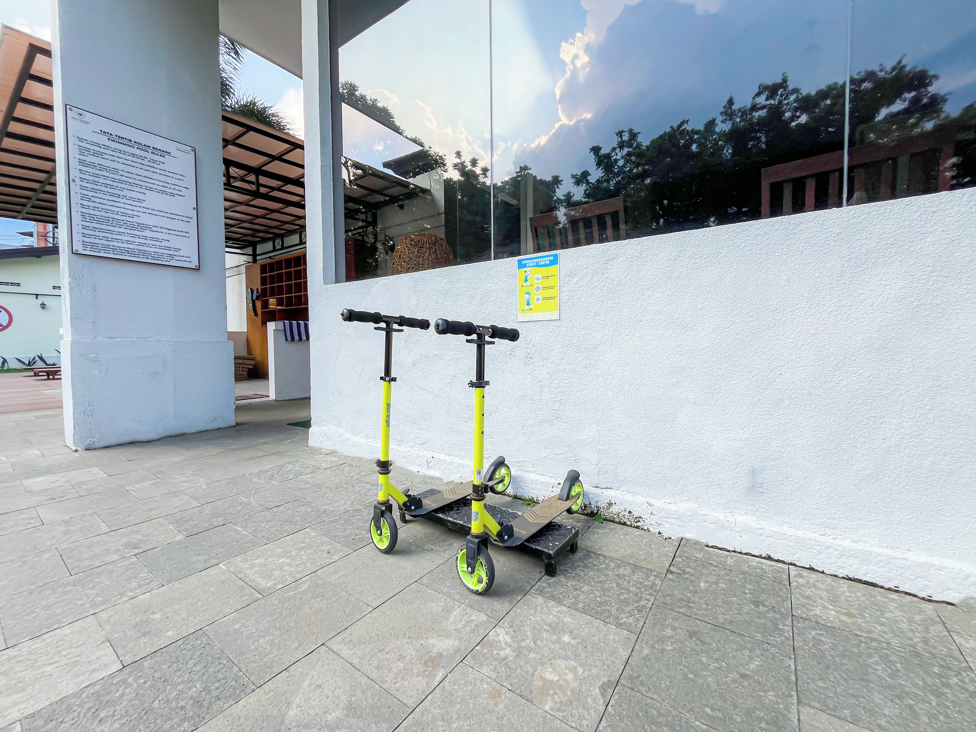 A scooter parked against a wall with a signboard and a poster nearby.