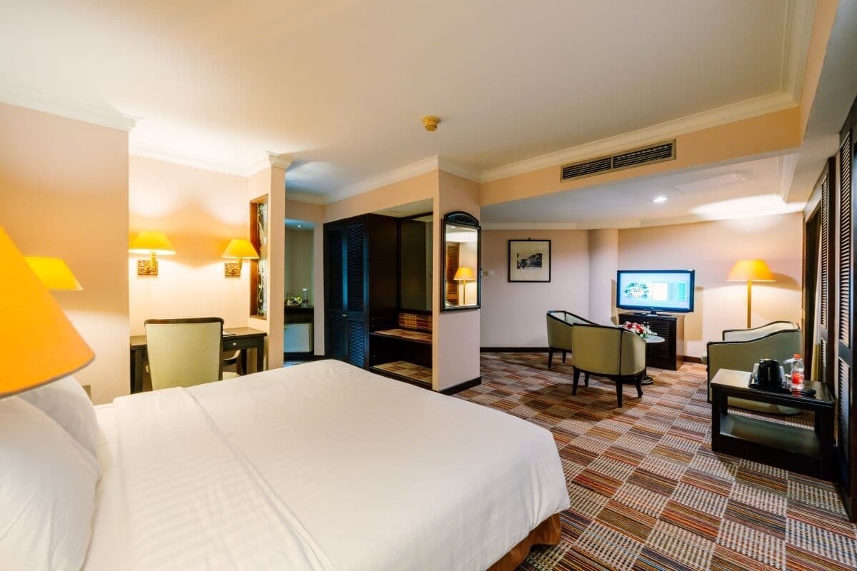 Een hotelkamer met een groot bed, een bureau, twee stoelen, een televisie en een kleine tafel met een lamp.