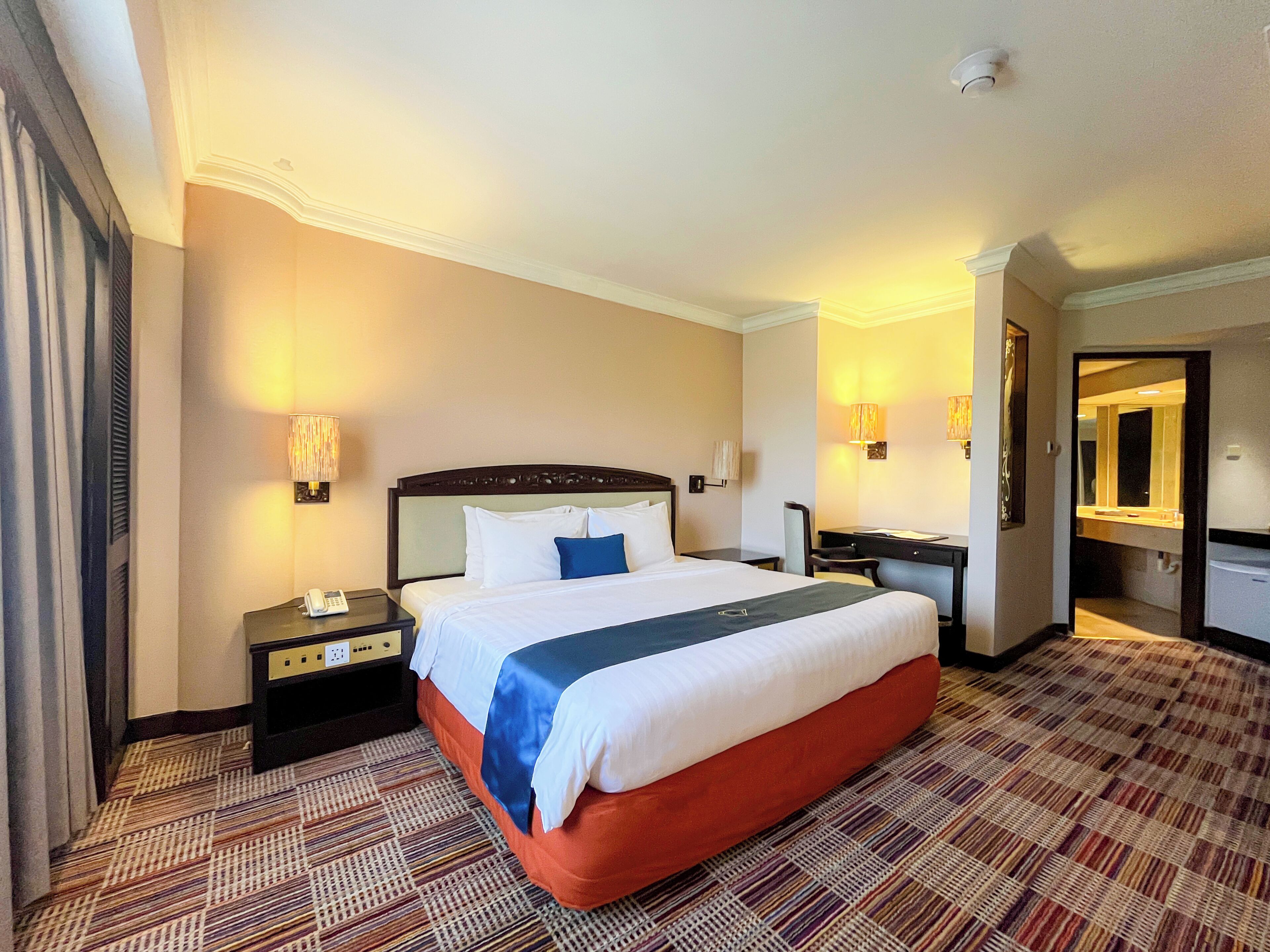 A hotel room with a large bed, a desk, a chair, a nightstand, and a mirror.