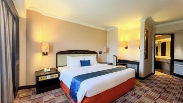 A hotel room with a large bed, a desk, a chair, a nightstand, and a mirror.