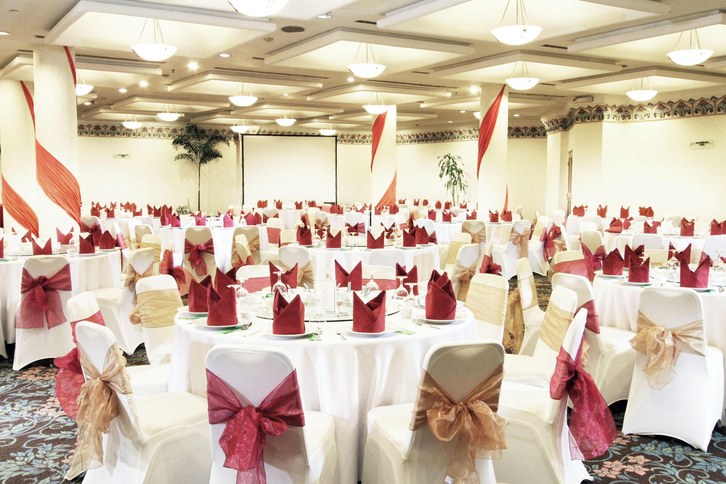 A banquet hall with round tables, white chairs, and red napkins.
