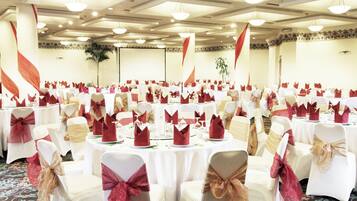 A banquet hall with round tables, white chairs, and red napkins.