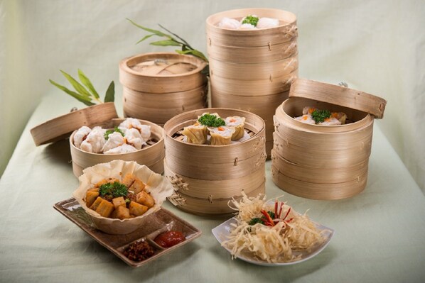 A variety of dim sum dishes in bamboo steamers and on plates, including dumplings and rolls, with a small bowl of sauce and shredded vegetables.