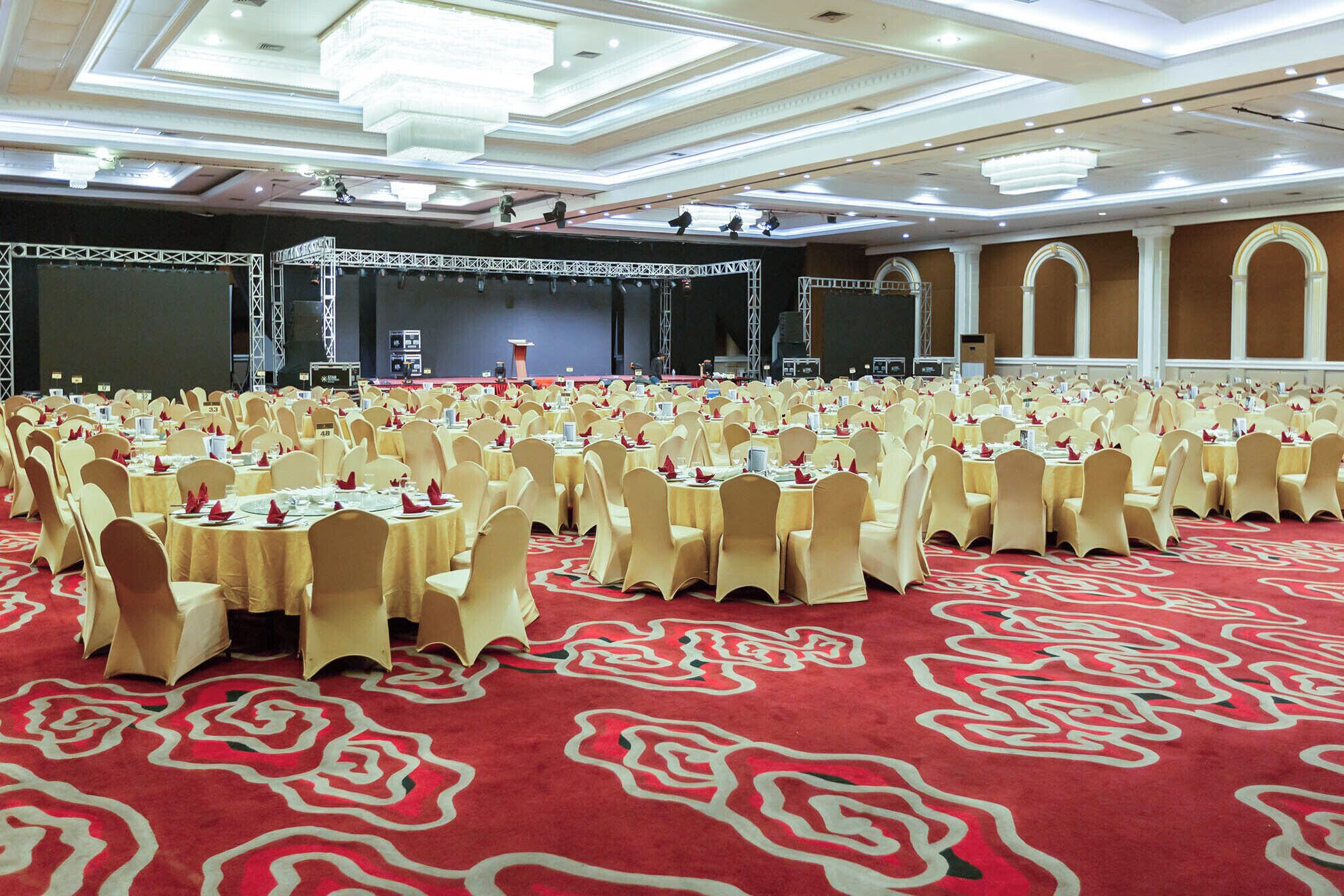 Un salón de banquetes con mesas redondas, sillas color beige y una alfombra roja con diseño floral.