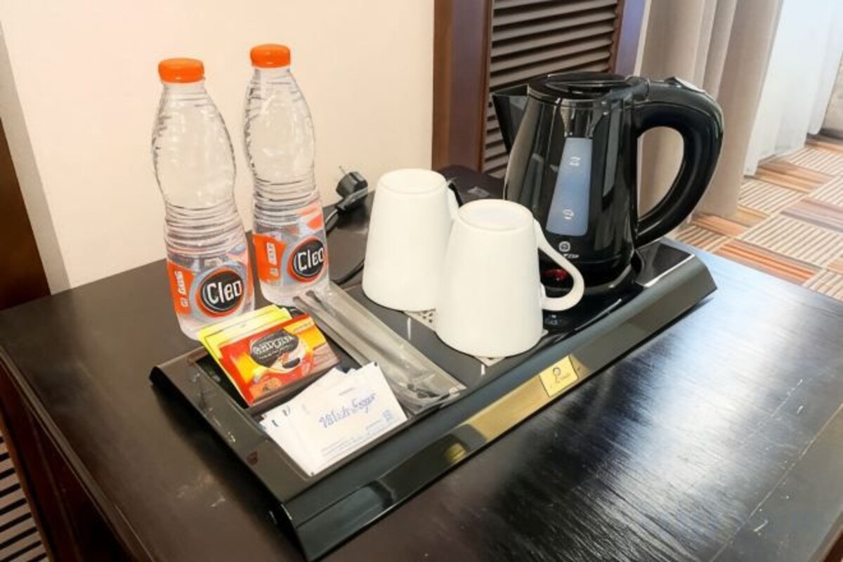 A hotel room's coffee station with two bottles of water, two white cups, a packet of sugar, and a coffee maker.