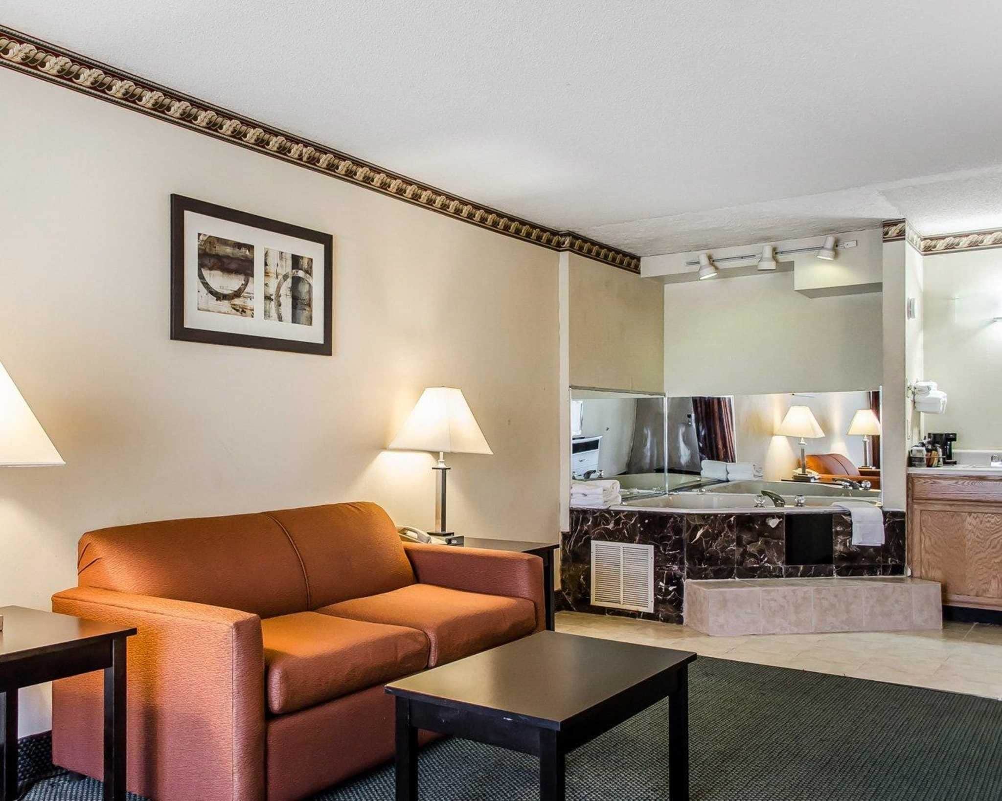 A hotel room with a sofa, a small table, a mirror, a sink, and a countertop.