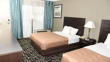 A hotel room with a large bed, a smaller bed, a desk, a chair, a lamp, and a painting on the wall.