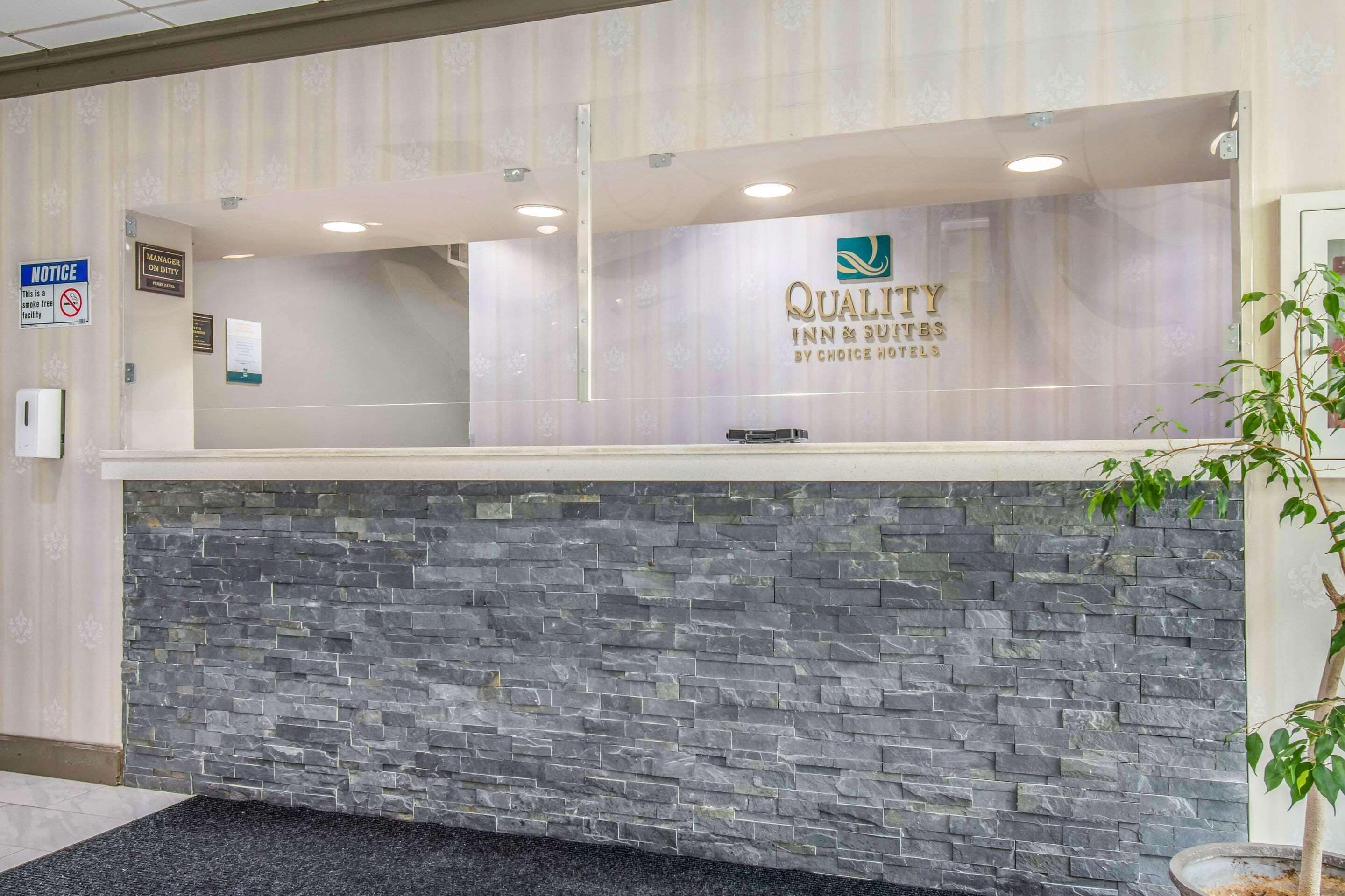 A reception desk with a stone wall, a sign for the Quality Inn & Suites, and a notice about the manager being on duty.