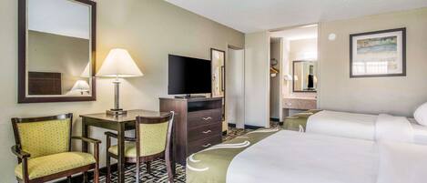 Habitación de hotel con una cama grande, un escritorio con silla, televisión, cómoda y baño visible a través de una puerta abierta.