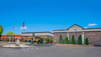 A commercial building with a parking lot, a fountain, and a flagpole.