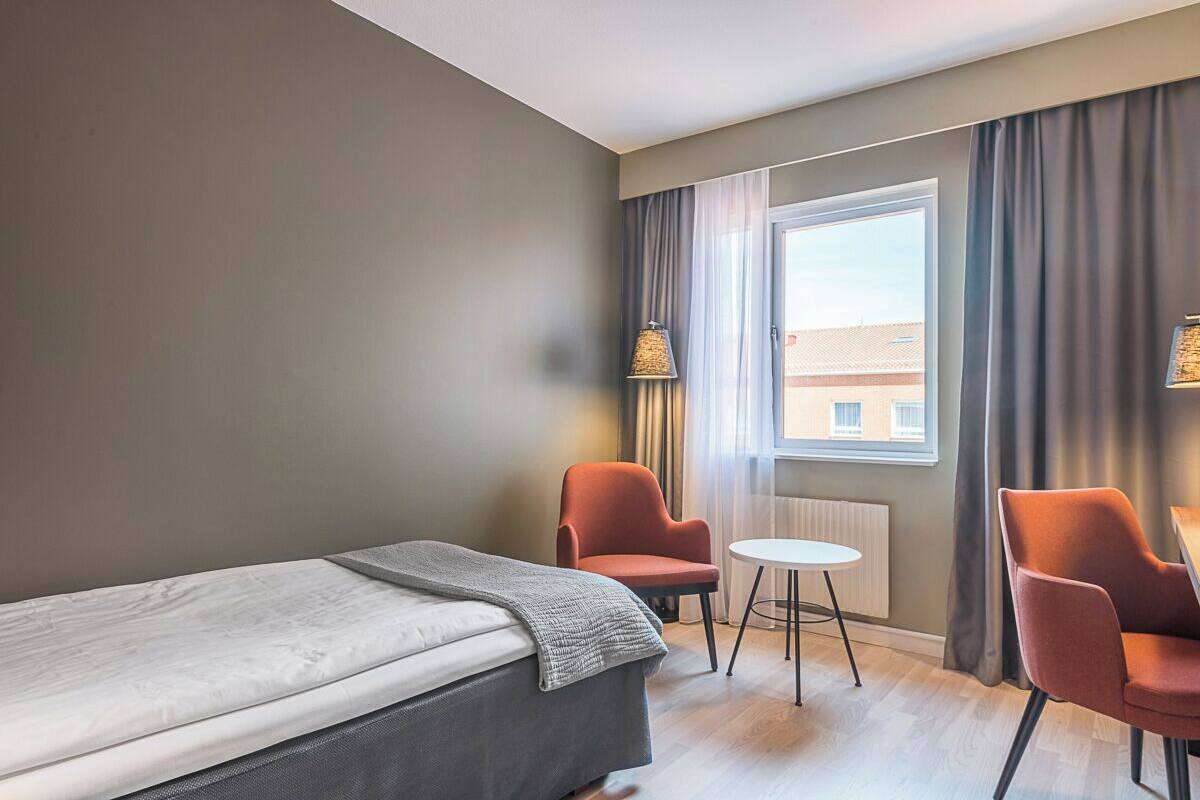 A hotel room with a bed, two chairs, a small table, and a window with curtains.