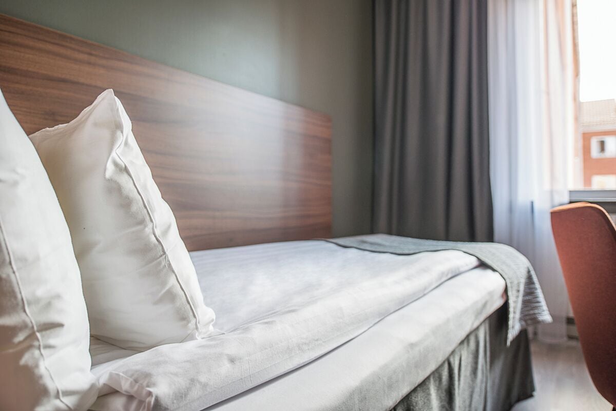 Una cama bien hecha con tablero de madera, una manta gris y almohadas blancas en una habitación de hotel.