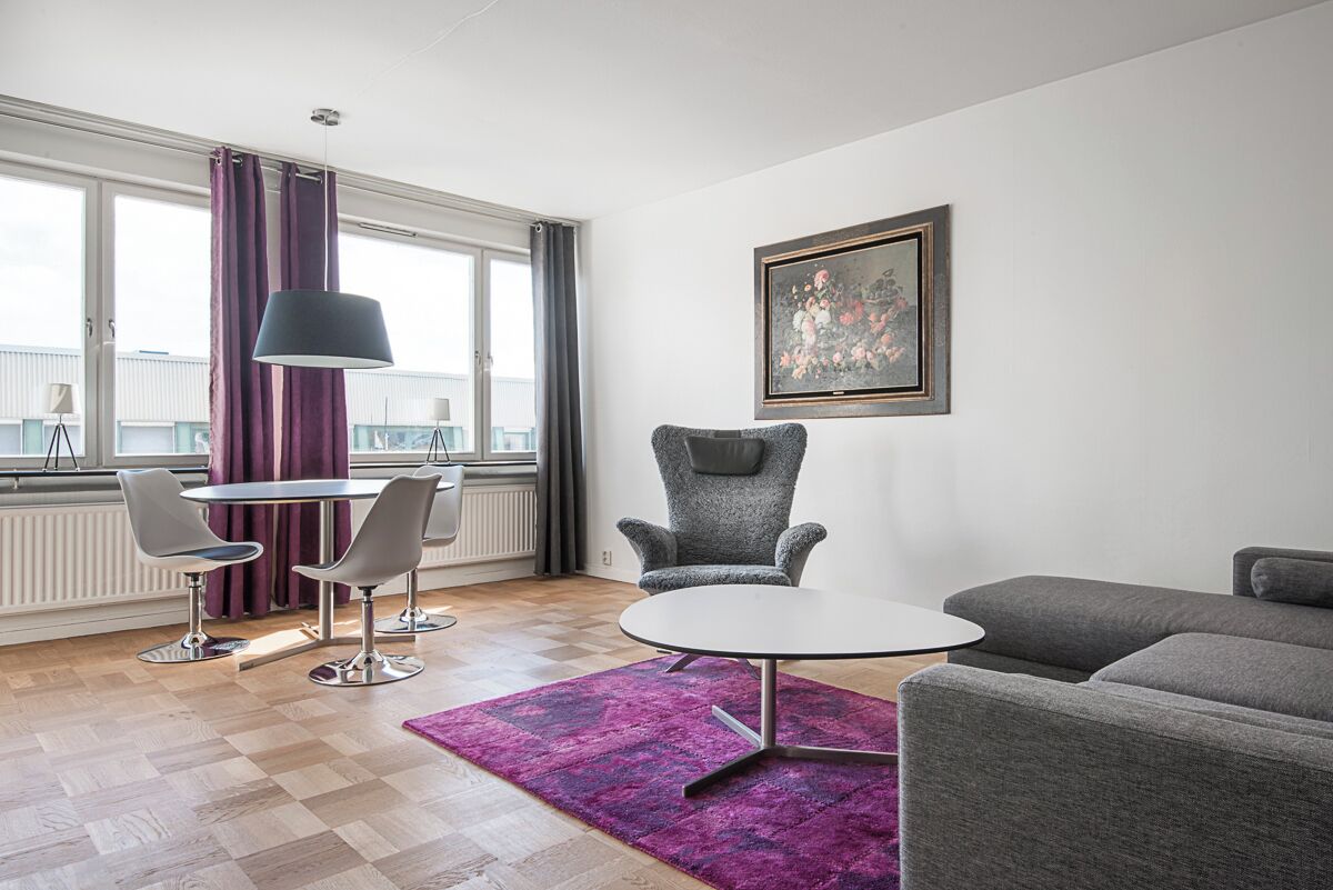 A modern living room with a round table, two grey chairs, a grey armchair, and a grey sofa.
