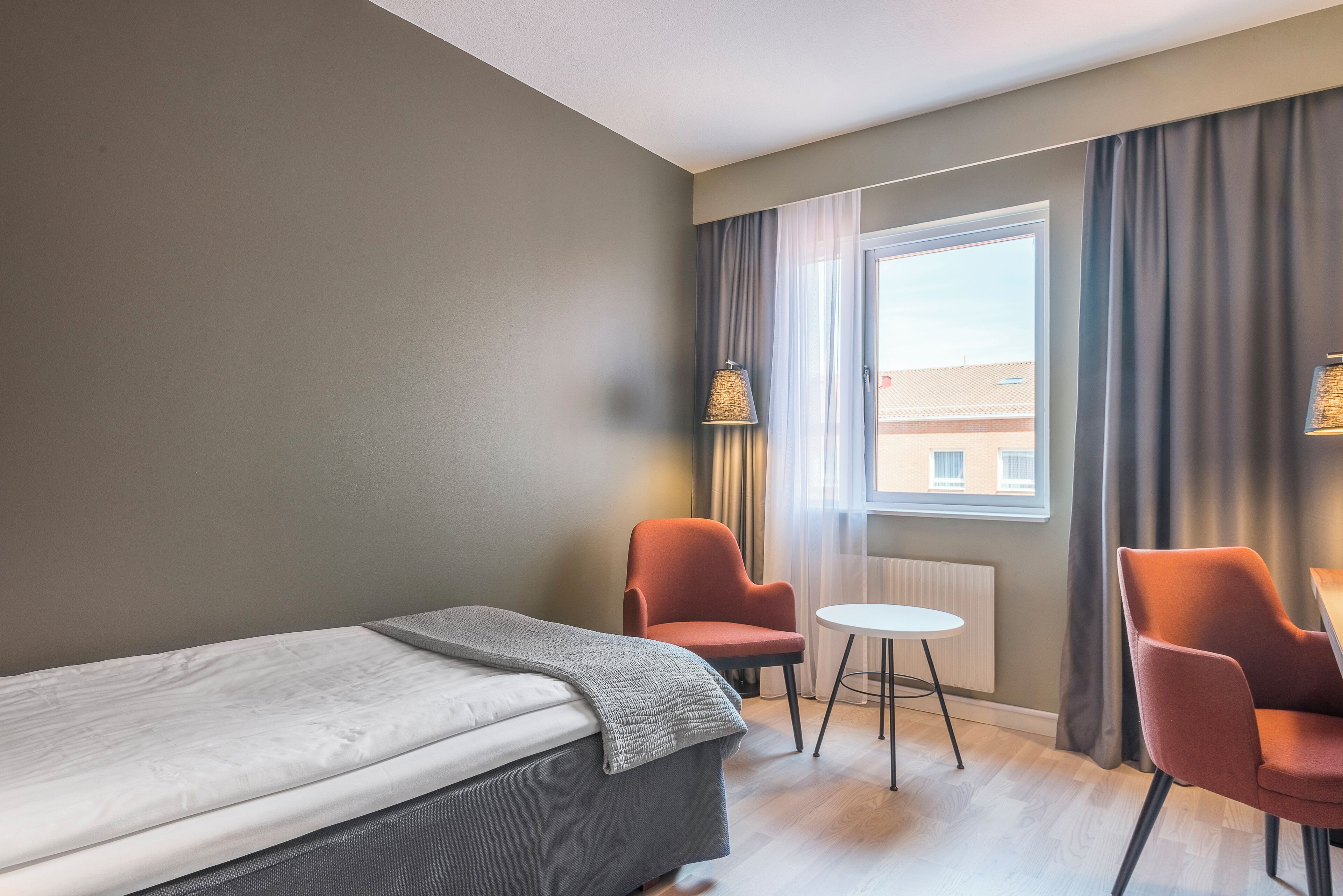 A hotel room with a bed, two armchairs, a small table, and a window with curtains.