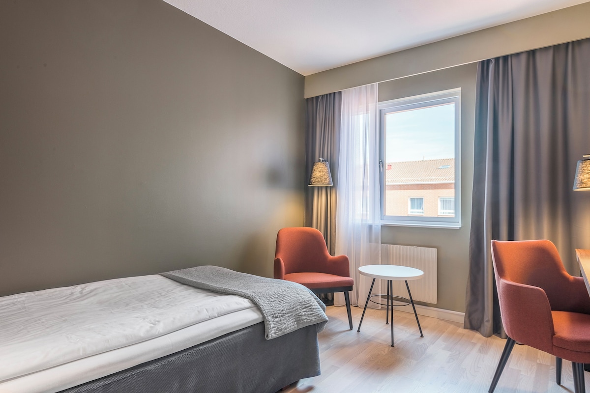 A hotel room with a bed, two armchairs, a small table, and a window with curtains.