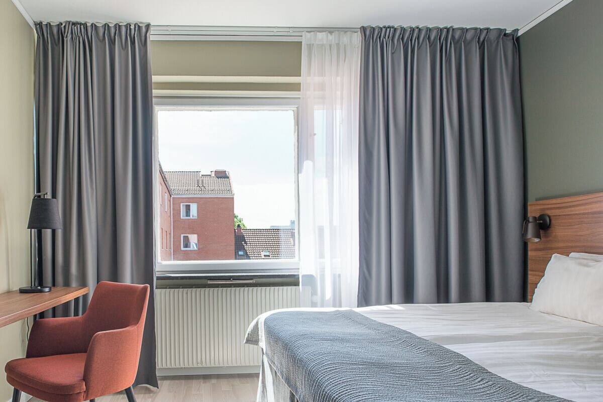 A hotel room with a bed, a desk, a chair, and a window with curtains.