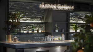 A modern bar area with a sleek design, featuring a unique glass chandelier, a variety of glassware, and a well-stocked bar. - ProfilHotels Grand Kristianstad (Kristianstad)