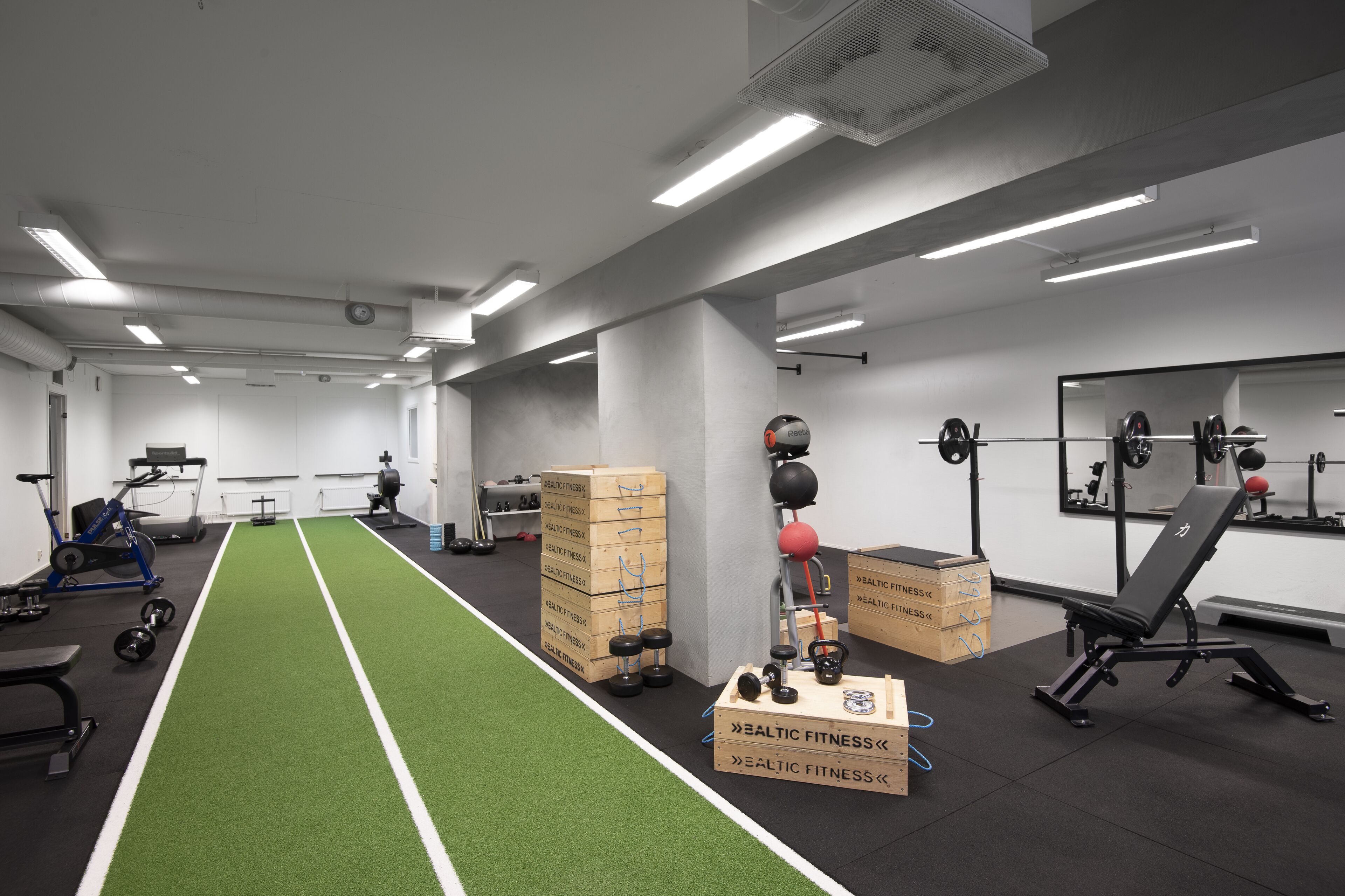 A gym with a green turf running track, weightlifting equipment, and exercise machines.