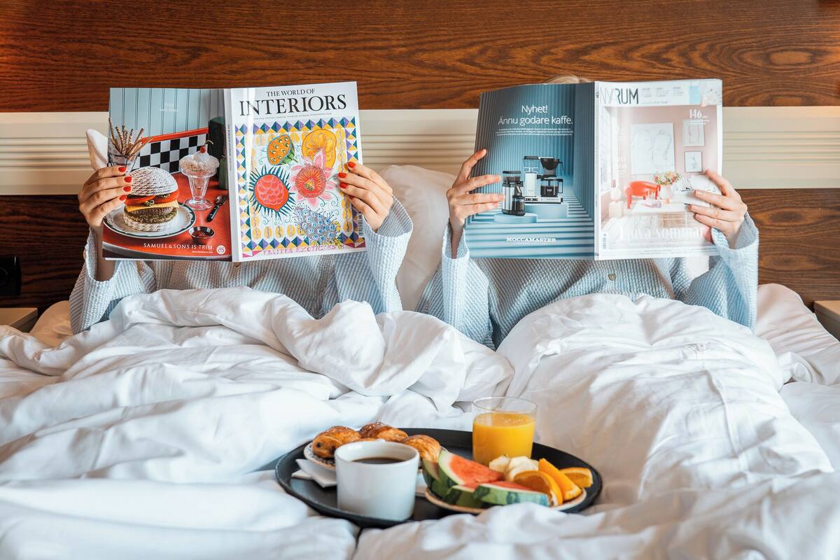 Two people reading books on a bed with breakfast.