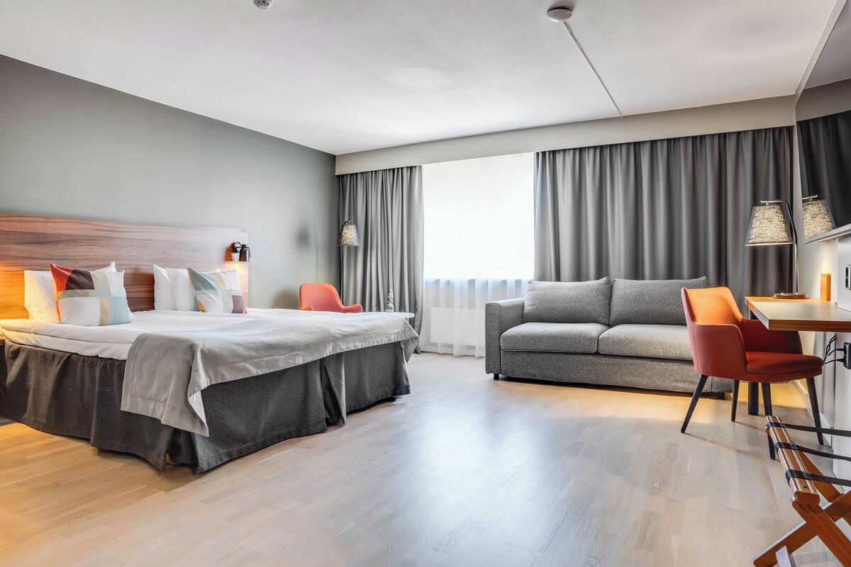 A modern hotel room with a bed, a sofa, a desk, and a chair.