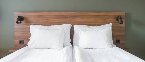 A neatly made bed with white linens and a grey textured bedspread, positioned against a green wall with a wooden headboard and two wall-mounted light fixtures.