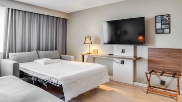 A modern hotel room with a bed, a desk, a TV, and a wooden headboard.
