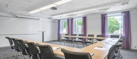 A conference room with a long table, chairs, a projector screen, and windows with curtains.