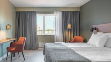 A hotel room with a bed, a desk, a chair, and a view of the outside.