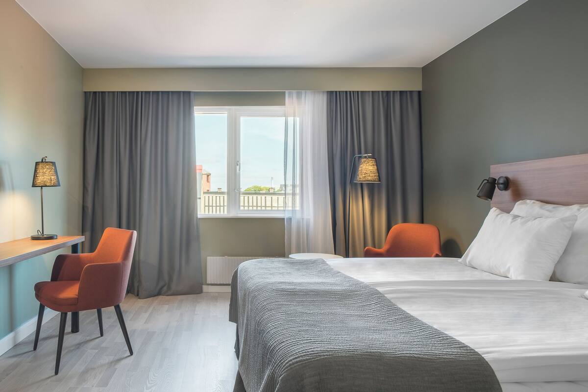 A hotel room with a bed, a desk, a chair, and a view of the outside.
