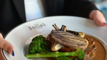 En person som håller i en tallrik med en bit kött, broccoli och sås.