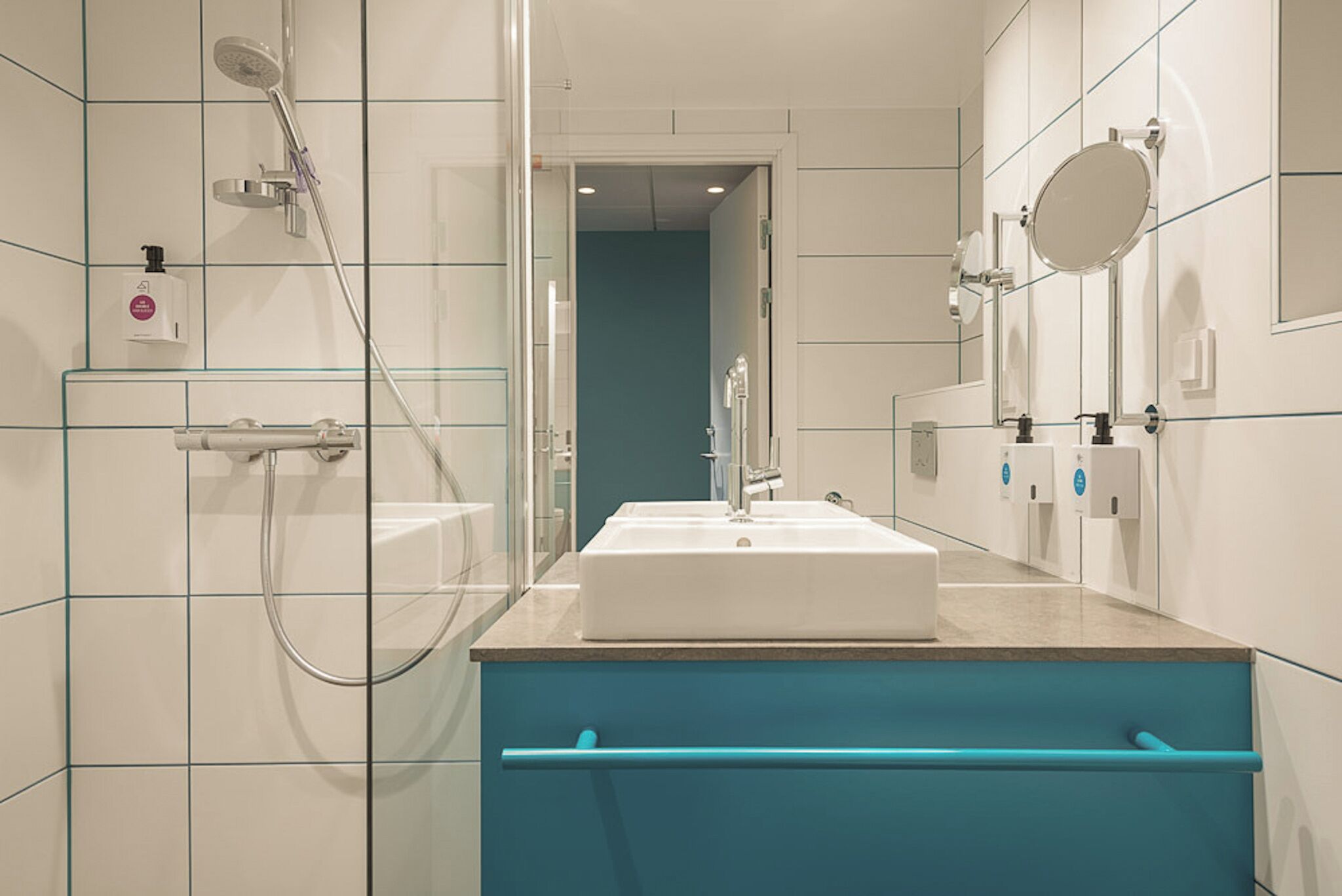 A modern bathroom with a glass shower enclosure, a white sink, and a blue vanity.