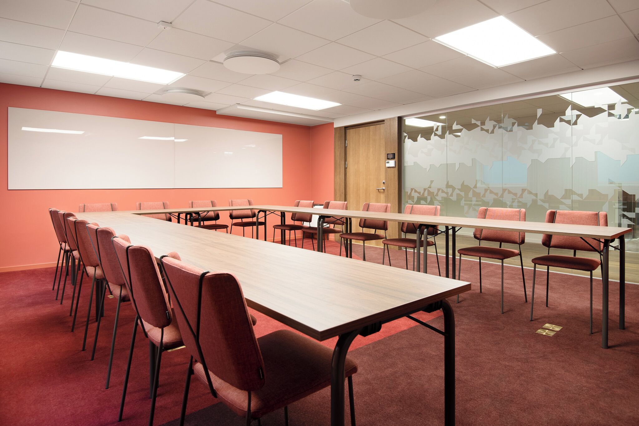 Un salón de conferencias con una mesa larga, varias sillas, una pizarra y un panel de vidrio con vista a la ciudad.